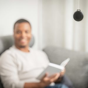 Svart radondosa hängande i ett rum med suddig person som sitter i en soffa och läser bok i bakgrunden