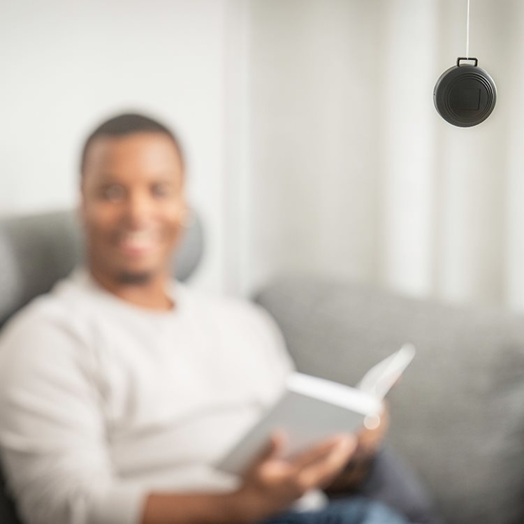 Svart radondosa hängande i ett rum med suddig person som sitter i en soffa och läser bok i bakgrunden